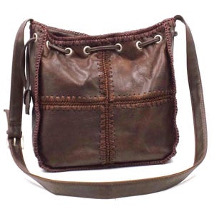 Puede incluir: Bolso de hombro de cuero marrón con diseño de patchwork. El bolso tiene un cierre de cordón con ojales metálicos y una correa larga ajustable. Las costuras y los ribetes son de un tono marrón más oscuro.