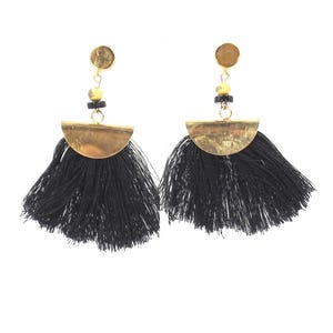 May include: A pair of black tassel earrings with gold-colored accents. Each earring features a gold-colored stud, a small cluster of yellow and black beads, and a half-circle gold-colored metal piece above the black tassels. The earrings are set against a white background.