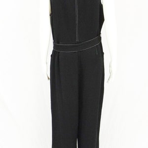 May include: Black sleeveless jumpsuit with a white top stitch detail and a belt. The jumpsuit has a wide leg and a relaxed fit.