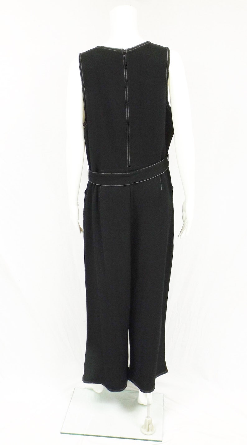 May include: Black sleeveless jumpsuit with a white top stitch detail and a belt. The jumpsuit has a wide leg and a relaxed fit.