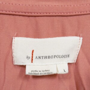May include: A white tag with the text "by ANTHROPOLOGIE" and "made in turkey / fabriqu&eacute; en turquie". The tag is sewn onto a pink fabric.