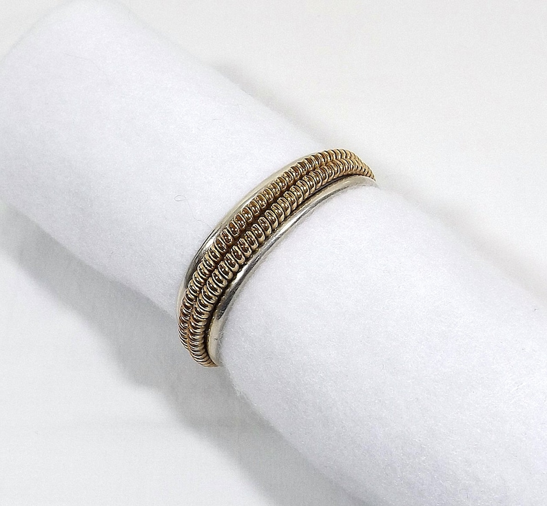 May include: A silver and gold ring with a braided design. The ring is made of two bands, one silver and one gold, that are braided together.