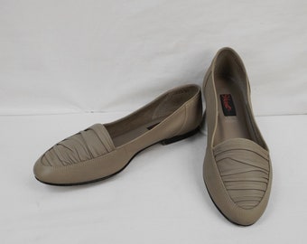 Puede incluir: Un par de zapatos planos de cuero beige con un detalle fruncido en la punta. Los zapatos están etiquetados con "Quest" en el interior.