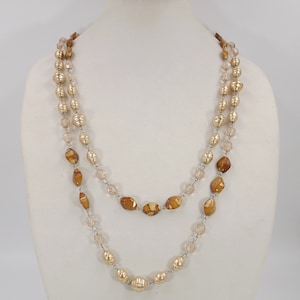 Puede incluir: Un collar de doble cadena con cuentas de color marrón y crema. El collar está hecho de vidrio y perlas falsas.