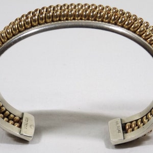 May include: A silver and gold bangle bracelet with a braided design. The bracelet is marked "H.L. Davis" on the inside.