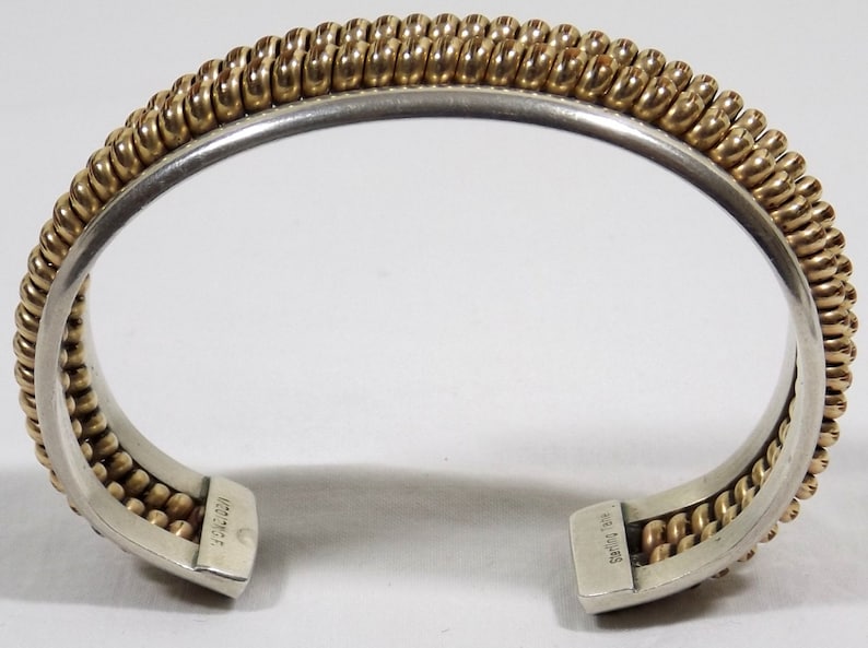 May include: A silver and gold bangle bracelet with a braided design. The bracelet is marked "H.L. Davis" on the inside.