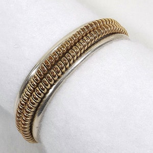 May include: A silver and gold ring with a textured design. The ring is made of two bands, one silver and one gold, that are intertwined.