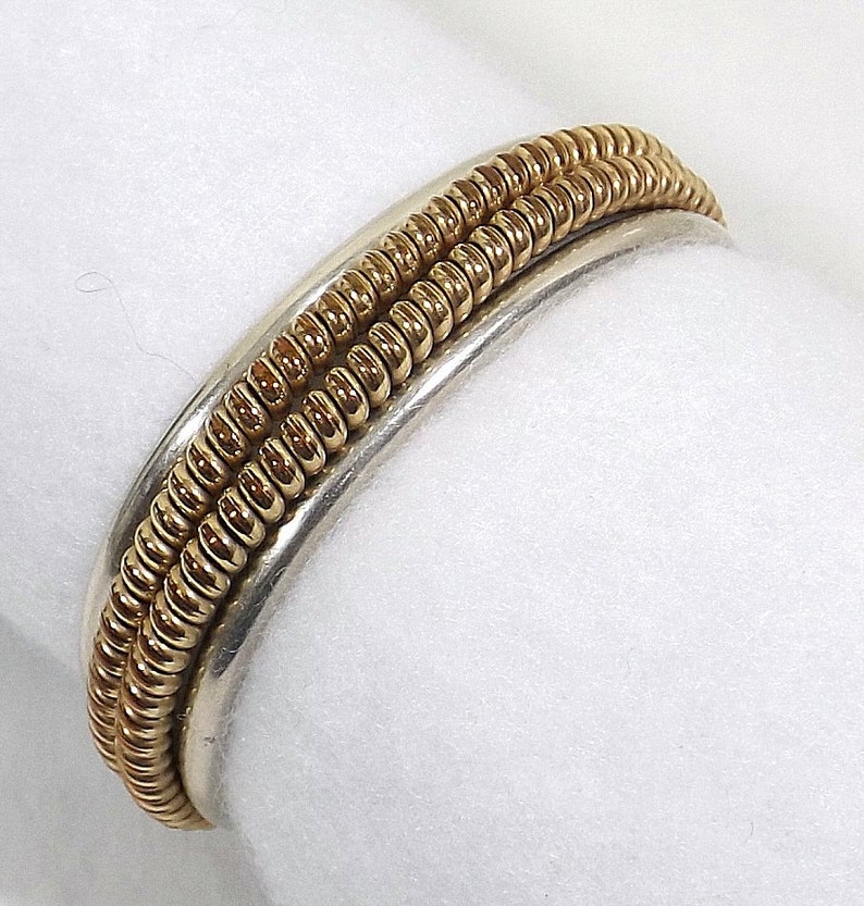 May include: A silver and gold ring with a textured design. The ring is made of two bands, one silver and one gold, that are intertwined.