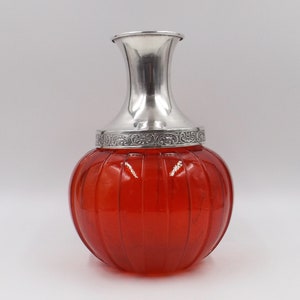 May include: A red glass vase with a silver top and a decorative design. The vase has a ribbed texture and a round shape.