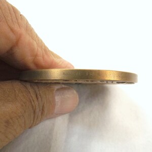 Puede incluir: Primer plano del borde de una medalla de bronce con la inscripci&oacute;n "BRONZE TIN" visible.