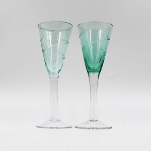 May include: Two clear green glass shot glasses with a swirl design. The glasses have a long stem and a wide base.