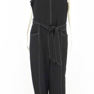 May include: A black sleeveless jumpsuit with a white top stitch detail. The jumpsuit has a wide belt and pockets.