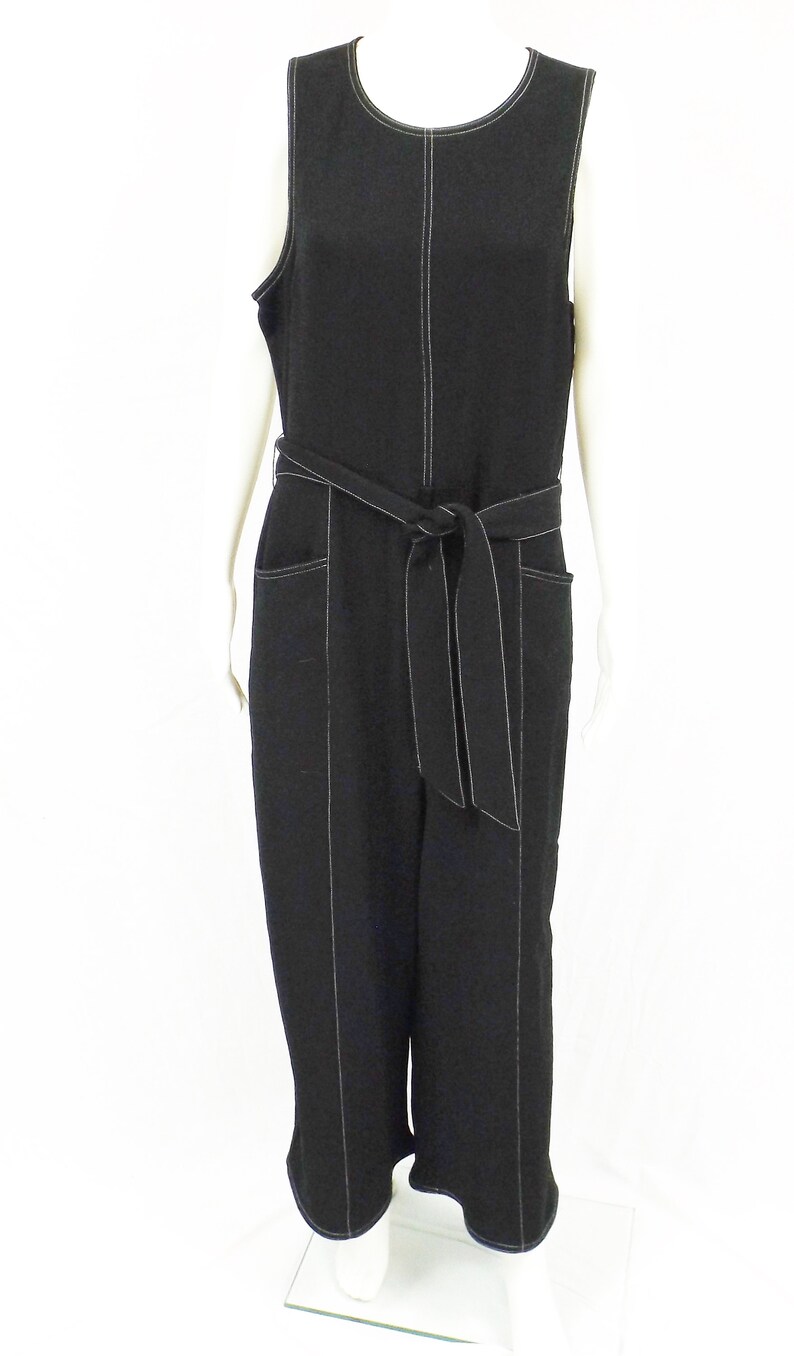 May include: A black sleeveless jumpsuit with a white top stitch detail. The jumpsuit has a wide belt and pockets.