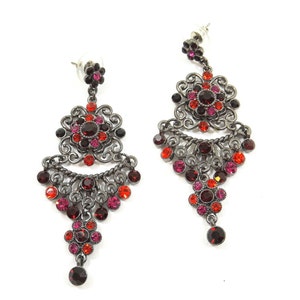 May include: A pair of dangle earrings with a silver tone finish. The earrings feature a large, ornate flower design with red, pink, and black crystals. The earrings are approximately 3 inches long.