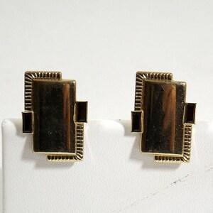 May include: A pair of gold-toned earrings with a rectangular design. Each earring features a dark red stone set in the center.