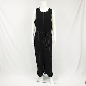 May include: Black sleeveless jumpsuit with a wide black belt and white stitching detail. The jumpsuit has pockets on the front and a wide leg.