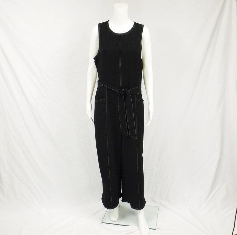 May include: Black sleeveless jumpsuit with a wide black belt and white stitching detail. The jumpsuit has pockets on the front and a wide leg.