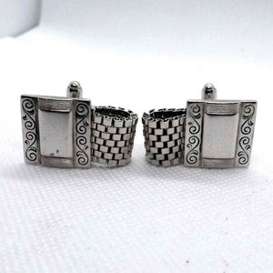 May include: A pair of silver cufflinks with a square design. The cufflinks feature a chain-like detail and a decorative border.