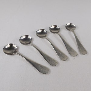 May include: Five silver teaspoons with ornate handles. The spoons are all the same size and have a rounded bowl. The handles are decorated with a floral pattern.