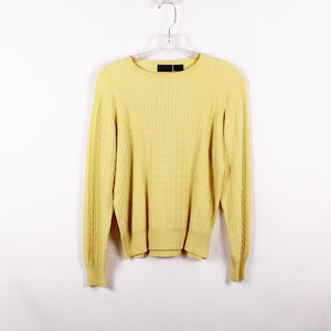 May include: A pale yellow cable knit sweater with long sleeves and a crew neck.