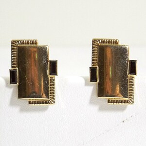 May include: A pair of gold earrings with black square-shaped stones set in a geometric design.