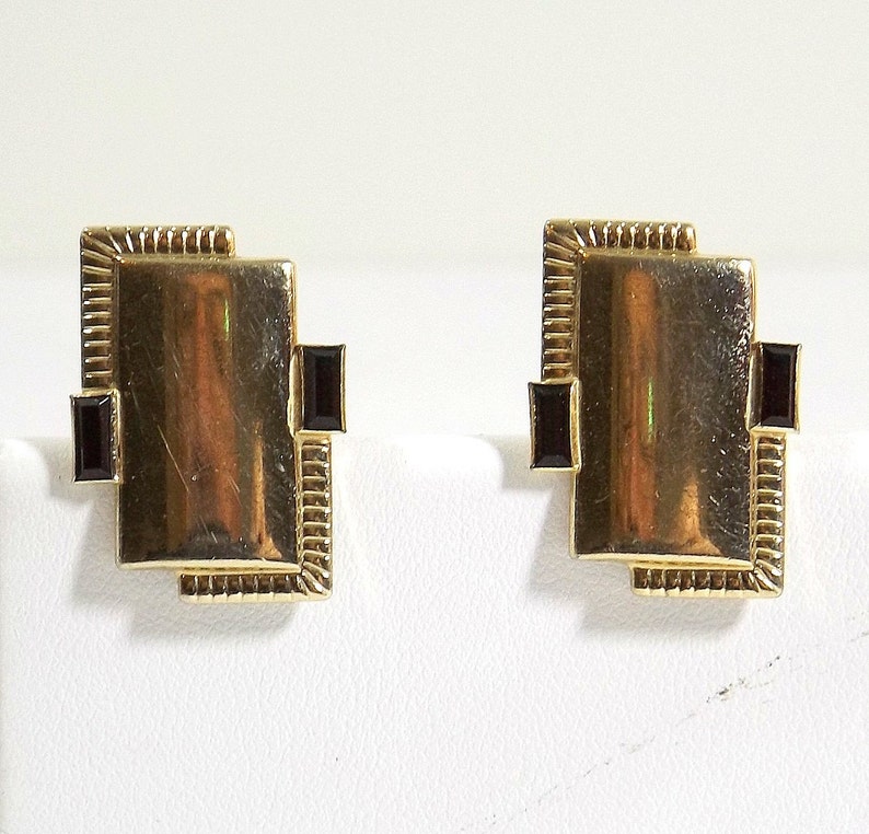 May include: A pair of gold earrings with black square-shaped stones set in a geometric design.