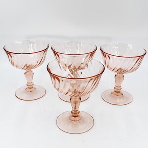 Könnte beinhalten: Set aus vier rosafarbenen Champagnergläsern aus Glas mit einem Spiralmuster. Die Gläser haben einen klaren Fuß und eine rosafarbene Schale.
