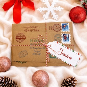 May include: A brown kraft paper envelope featuring North Pole branding, a Santa Claus approved stamp, and two postage stamps. The envelope is tied with red and white twine and includes a white gift tag with the name Jessica written in red script.