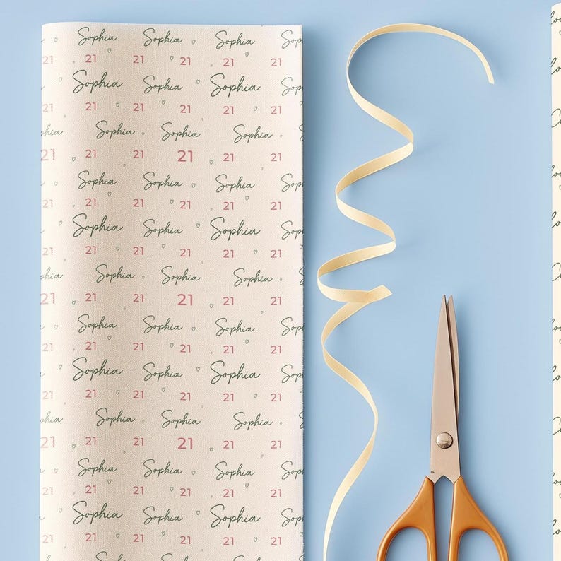 May include: A roll of wrapping paper with the name "Sophia" and the number "21" printed repeatedly in a pattern. A pair of gold-handled scissors and a cream-colored ribbon are on a light blue background.