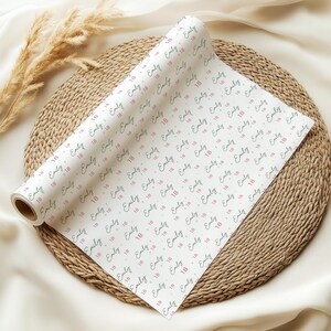 May include: A roll of white wrapping paper featuring a repeating pattern of the name Emily in a dark script font interspersed with the number 18 in a pink sans-serif font, arranged in diagonal rows across the surface of the paper.