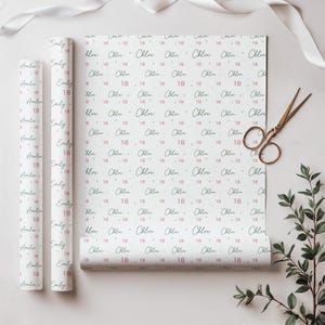 May include: White wrapping paper featuring a repeating pattern of the names Chloe and Emily in a dark script font, interspersed with the number 18 in a light pink color and small gray dots. Two rolls of the paper are shown alongside a flat sheet.