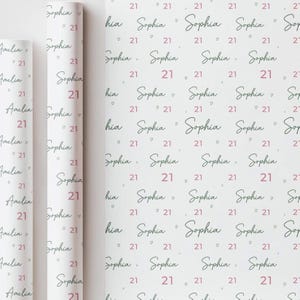 May include: White wrapping paper with a repeating pattern of the name "Sophia", the number "21", and small pink hearts. Rolled paper on the left shows the name "Amelia" and the number "21".