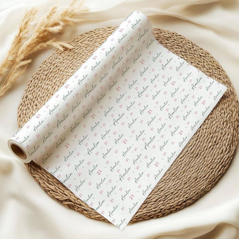 May include: White wrapping paper roll with a repeating pattern of the name "Amelia" and the number "21" in a handwritten style. The paper is on a woven mat with dried plants.