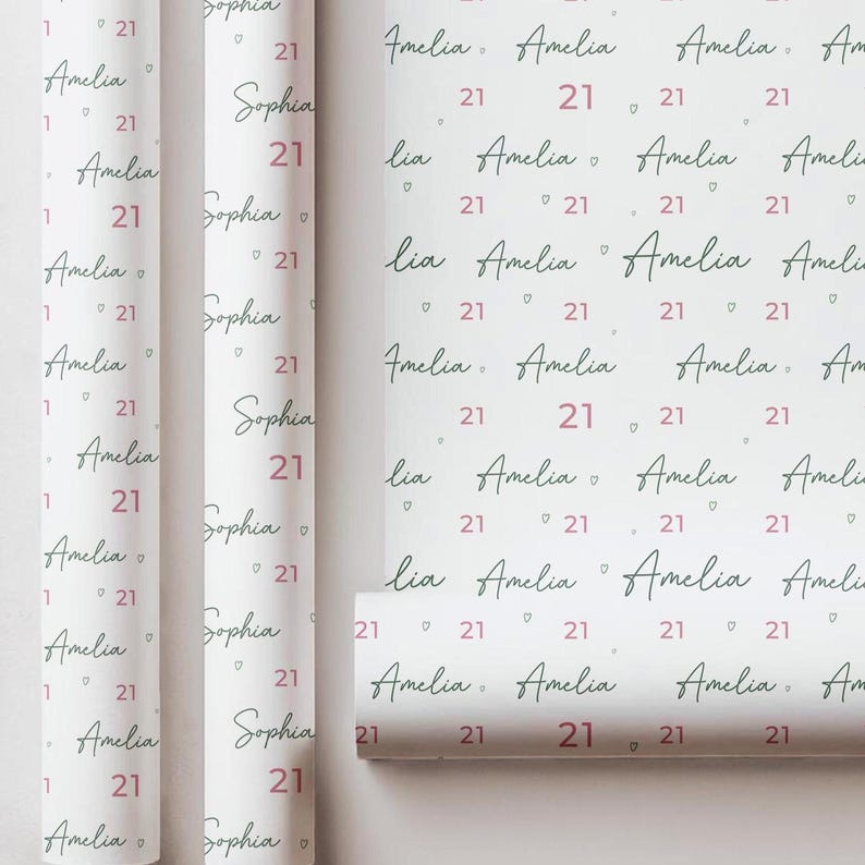 May include: White wrapping paper with a repeating pattern of the name "Amelia" in a handwritten font, the number "21" in a pink hue, and the name "Sophia". The paper is rolled and ready for use.