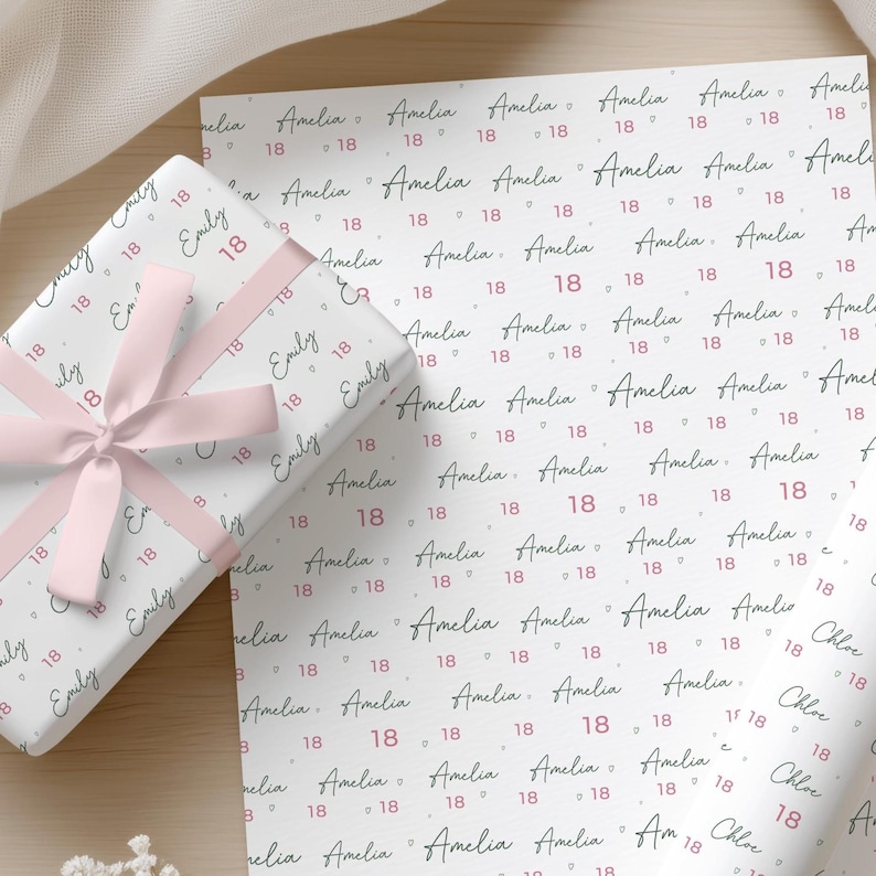 May include: White wrapping paper featuring a repeating pattern of the name Amelia in black cursive script, interspersed with the number 18 in pink, wrapped around a gift box tied with a light pink satin ribbon bow.