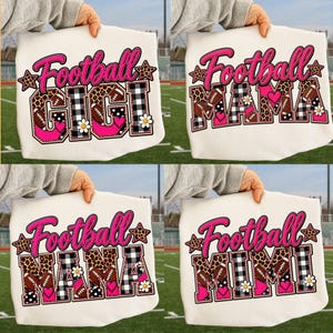 May include: Four white sweatshirts featuring graphic designs with the text Football GIGI, Football MAMA, Football NANA, and Football MIMI. The letters incorporate leopard print, black and white buffalo plaid, footballs, pink hearts, and white flowers.