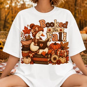 May include: A white t-shirt featuring a graphic of a duck wearing a hat and scarf, reading a book. The text reads Booked For Fall, Cozy Days, Pumpkin Spice, and Sweater Weather. The design includes pumpkins, autumn leaves, and a coffee cup.