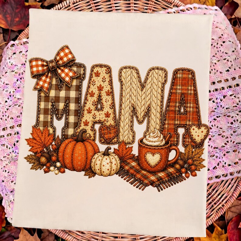 May include: A white t-shirt featuring the word MAMA in large, decorative letters. The letters have patterns including brown plaid, autumn leaves, cable knit, and orange plaid. A plaid bow sits on the first M, with pumpkins and a mug of cocoa below.