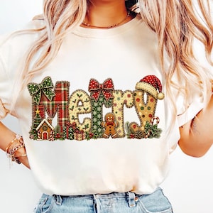 以下が含まれることがあります： クリーム色のTシャツで、Merryという文字が大きく装飾的に描かれています。各文字は、赤のチェック柄、緑のヒイラギ、金の雪の結晶、ジンジャーブレッドマンなどの祝祭的な模様で埋め尽くされており、リボンやサンタの帽子で飾られています。