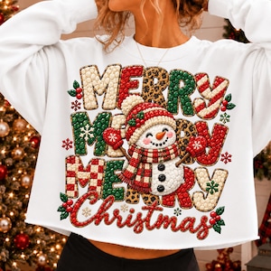 May include: A white long-sleeve sweatshirt featuring a large graphic print of a snowman wearing a red and white plaid scarf and hat. The text "MERRY MERRY MERRY Christmas" is displayed in a textured, multi-colored pattern with holly accents.