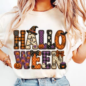 May include: A cream-colored t-shirt featuring the word HALLOWEEN in large, block-style letters. Each letter is filled with various Halloween-themed patterns including orange and black plaid, pumpkins, ghosts, bats, spiderwebs, and a witch hat.