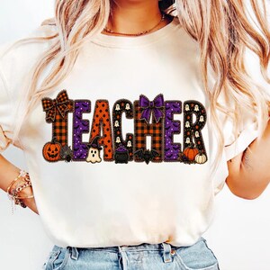Può includere: Una t-shirt color crema con la parola TEACHER in grandi lettere stampatello. Ogni lettera presenta un motivo unico a tema Halloween, tra cui quadri arancioni e neri, viola con fantasmi e arancione con pois neri, decorata con fiocchi.