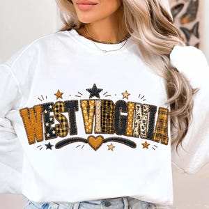 May include: A white long-sleeve sweatshirt featuring the text WEST VIRGINIA in large, block-style letters. Each letter has a unique pattern, including yellow paisley, black and yellow plaid, and floral prints. Small stars and a heart are included.
