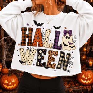Puede incluir: Una sudadera blanca de manga larga con la palabra HALLOWEEN en letras grandes y estampadas. Las letras incluyen cuadros, lunares y estampados de leopardo, decoradas con pequeños gráficos de fantasmas, murciélagos y telarañas.