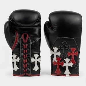 Puede incluir: Un par de guantes de boxeo de cuero negro con aplicaciones en forma de cruz rojas y blancas. El guante izquierdo tiene un cierre de cordones negro con ribete rojo, mientras que el derecho muestra un grupo de parches de cruces en rojo, blanco y negro.