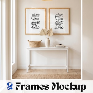 May include: Two rectangular wooden frames hanging on a wall, each containing white paper with the black text "place your design here". Below the frames is a white console table with a woven basket, a vase with dried palm leaves, and books.