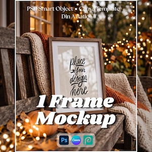 May include: A wooden picture frame mockup featuring a white mat board and the text "place YOUR design here" in black script. The frame rests on a wooden bench draped with a thick, textured cream and orange knit blanket, with soft bokeh lights.