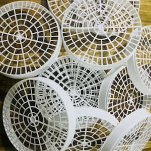 May include: A collection of white circular plastic grids featuring a radial and concentric pattern. Each piece has a raised outer rim and a structured lattice design with open square segments, arranged in an overlapping cluster.