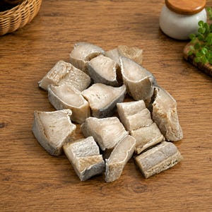 May include: A collection of raw, cubed fish pieces with a pale, off-white flesh and textured, grayish-brown skin. The pieces are irregular in shape and size, showing a firm, dense texture typical of salted or dried white fish fillets.