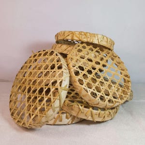May include: A stack of circular, light tan woven bamboo baskets featuring an open, crisscross lattice pattern. Each basket has a sturdy, reinforced rim and a flat, circular base, showcasing the natural texture and color of the bamboo material.